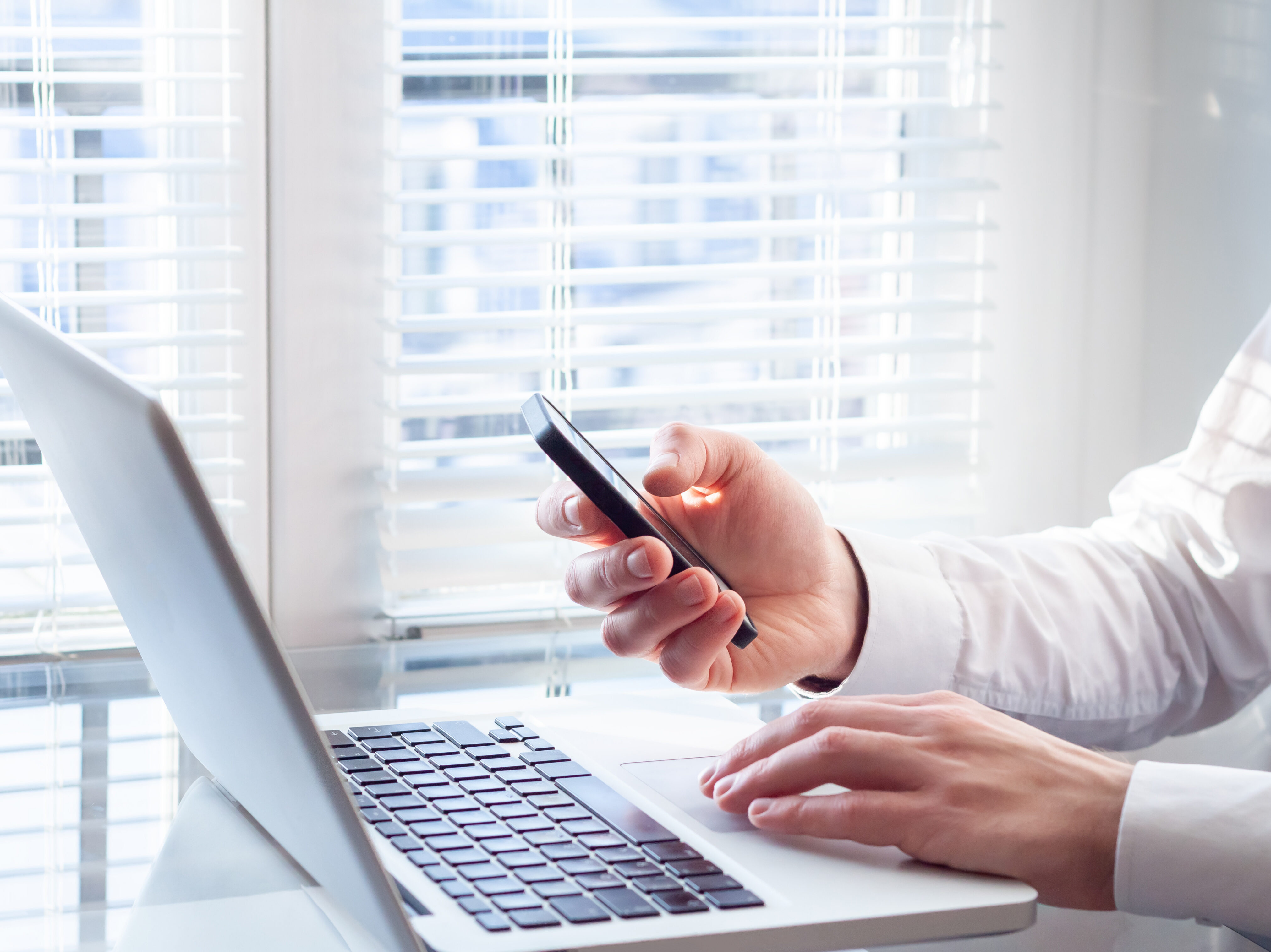 Businessman working with laptop and smartphone, bright office, f
